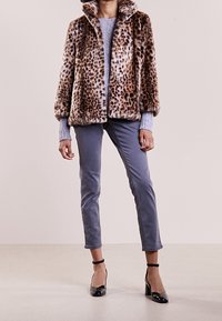 Leopardikuosi keinoturkis takki, pehmeä koostumus, pyöreä kaulus, yhdistettynä vaaleansinisiin housuihin ja mustiin korkokenkiin.