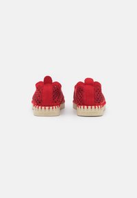 Scarpe rosse in suede con design perforato, suola beige a contrasto con bordi seghettati e tallone rinforzato per stabilità.