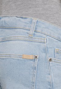Os jeans de denim azul claro têm uma cintura de altura média, costura amarela, etiqueta de couro com "L2W" e hardware prateado no bolso de trás.