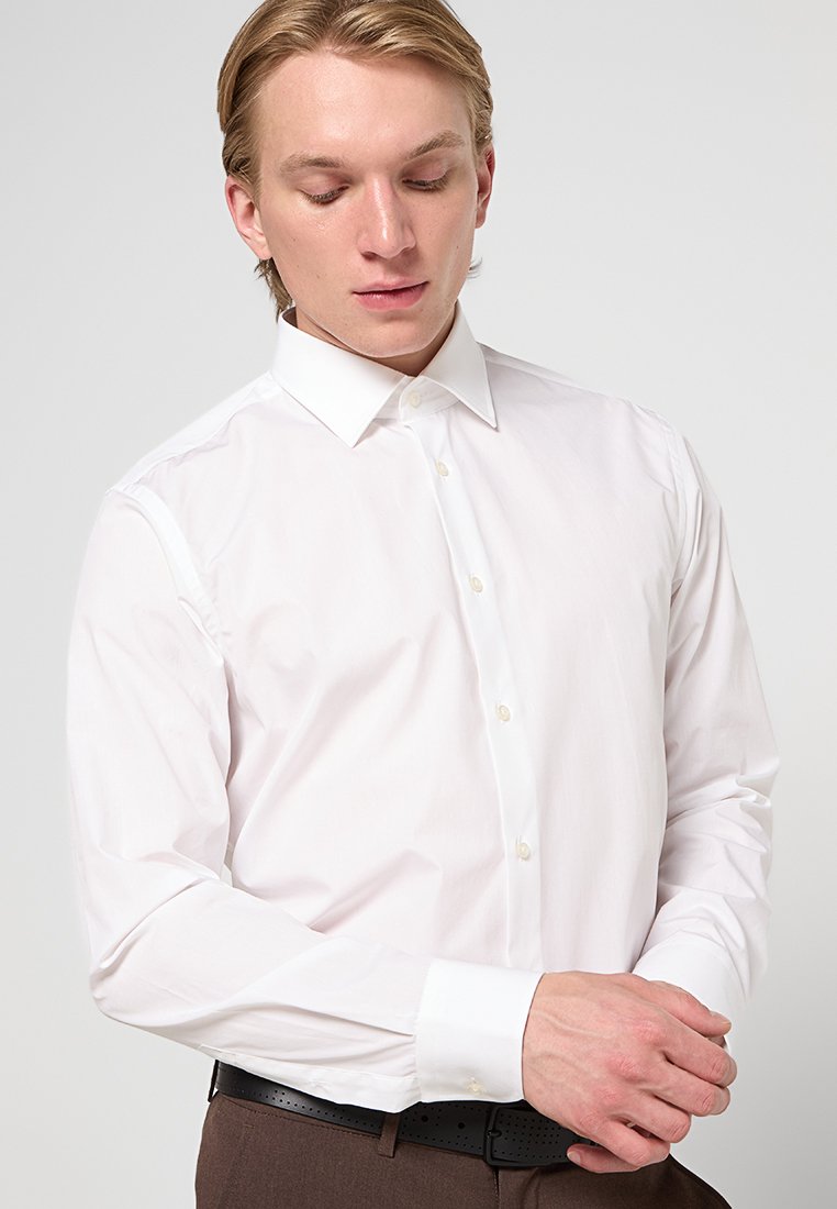 Chemise blanche à manches longues avec col italien, fermeture à boutons et texture lisse. Présente une coupe ajustée et un design minimaliste.