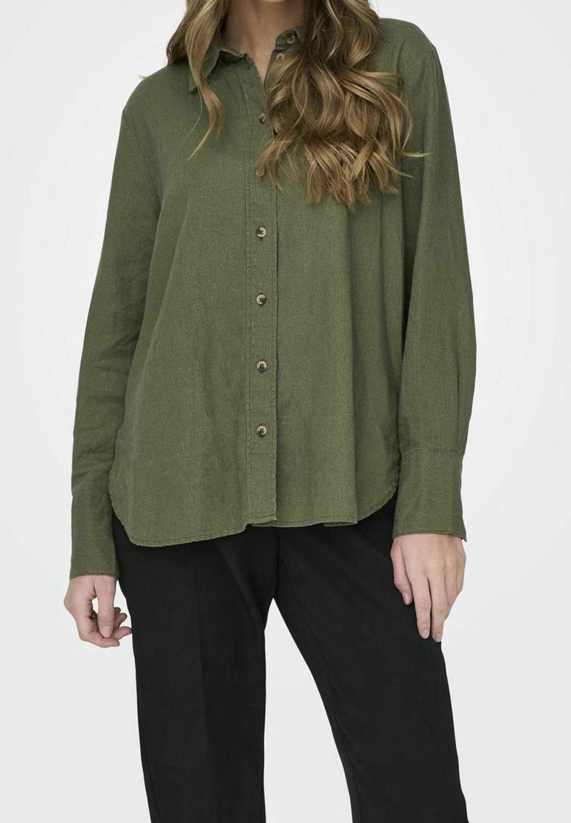 Chemise verte à boutons, en tissu texturé, dotée d'un col classique, de boutons sur le devant et de manches longues, associée à un pantalon noir.