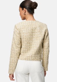 Giacca in paillettes dorate con finitura strutturata, scollatura rotonda e maniche lunghe. La parte posteriore presenta un design semplice senza chiusure visibili.