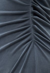 Σκούρο γκρι ύφασμα με κάθετη ρίγα που δημιουργεί μαζεμένες, υφασματικές πτυχές κατά μήκος μιας κεντρικής ραφής.