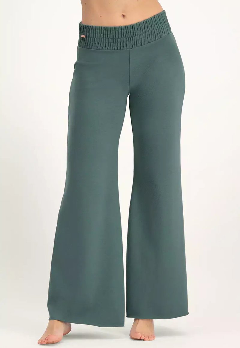 Vihreät leveälahkeiset housut, joissa on joustava vyötärö, käytössä paljain jaloin, ja ne ulottuvat puoliväliin vartaloa jalkoihin yksinkertaista taustaa vastaan.