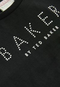 Melnas kokvilnas T-kreklas ar sudraba rotājumiem "BAKER" un "by TED BAKER". Īsas piedurknes, apaļa kakla izgriezums, gluda tekstūra.