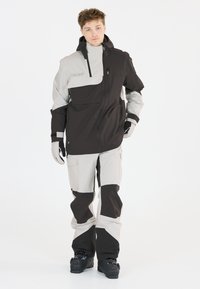 Ensemble de ski composé d'une veste et d'un pantalon en noir et gris clair, fabriqué en tissu imperméable. Il présente une capuche réglable, plusieurs poches et des accents renforcés.