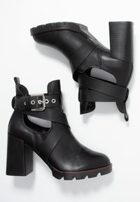 Botas de tobillo de cuero negro con un diseño de tacón grueso, que presentan correas entrelazadas, un corte lateral y accesorios de hebilla metálica.