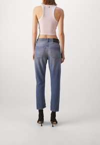 Top gris claro sin mangas, jeans azules de talle alto y tacones negros. Los jeans presentan un leve efecto ombré y doble bolsillo trasero.