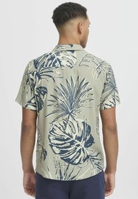 Chemise à manches courtes de couleur vert clair avec un motif floral bleu marine. Présente un col décontracté et un ourlet arrondi. Tissu léger avec une texture lisse.