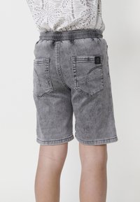 Los pantalones cortos de mezclilla gris cuentan con una cinturilla elástica, dos bolsillos traseros y un dobladillo enrollado. El material texturizado presenta un acabado desgastado.