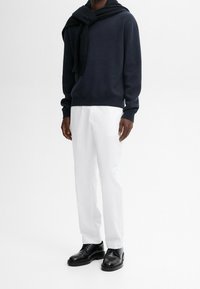 Marineblauer Strickpullover mit Schalkragen, weiße gerade Hose und schwarze Lederschuhe. Glatter Stoff mit klassischer Passform.
