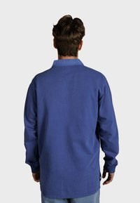 Blå långärmad skjorta med krage, ribbad textur och avslappnad passform. Synliga sömmar längs axlarna och sidorna.