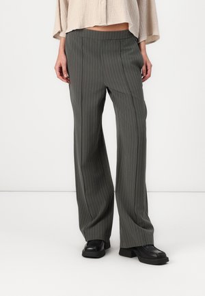 Pantalons à rayures grises avec une coupe décontractée, fabriqués dans un tissu lisse, dotés d'une taille plate et de jambes larges, associés à des chaussures noires épaisses.