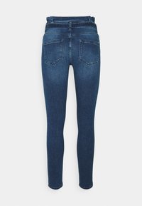 Jeans skinny azul oscuro mostrados desde la parte trasera con dos bolsillos traseros cosidos y bucles de cinturón visibles sobre un fondo blanco.