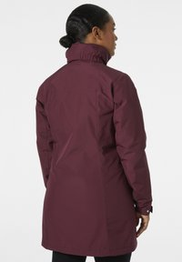 Abrigo acolchado burdeos con cuello alto, mangas largas y corte recto. Presenta un acabado de tela lisa y resistente al agua.