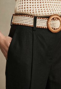 Pantaloni in lino neri con una cintura intrecciata beige e marrone, caratterizzata da una fibbia rotonda intrecciata, che mette in mostra texture a contrasto e un design strutturato.