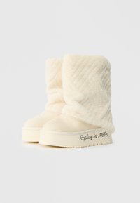 Kremkrāsas ziemas zābaki, izgatavoti no mīksta materiāla ar izšūtu rakstu. Biezā zole ir ar „Replay is More” zīmolu sānos.