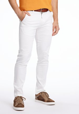 Pantalons blancs ajustés en mélange de coton, dotés de poches avant et d'une texture lisse. Portés avec des baskets en suède marron et un haut jaune.