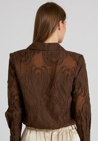 Giacca marrone ricamata con un motivo floreale a trama, maniche lunghe e colletto, caratterizzata da un design corto e tessuto trasparente.