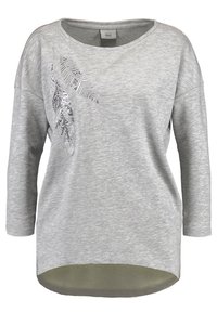 Blusa de manga larga gris claro con escote redondeado, hombros caídos y un diseño decorativo de hojas plateadas en la parte delantera. El dobladillo es ligeramente alargado.