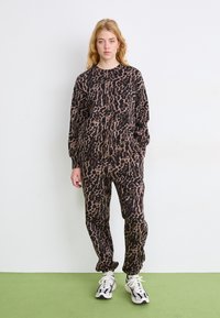 Trenirka z leopardskim vzorcem v rjavi in črni barvi, izdelana iz mehkega materiala, z dolgimi rokavi, manšetami na zapestjih in gležnjih ter ujemajočimi se supergami.