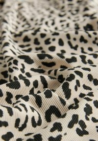 Tkanina w cętki z beżowym tłem, czarnymi plamami, teksturowanym ribbingiem i płynącą draperią.