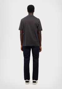 Dark gray short-sleeve t-shirt, relaxed fit, cotton material, paired with dark blue jeans, shown from the back. Neutral sneakers visible.
