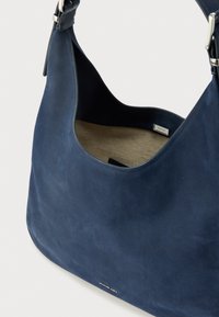 Mala de ombro azul em couro da Michael Kors com detalhes de fivela prateada e forro interior de tecido bege, mostrada em ângulo aproximado.