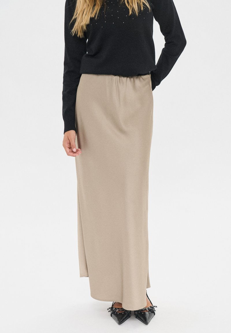 Falda beige de longitud media con cinturilla elástica y textura suave, combinada con un suéter negro y zapatos negros de punta.