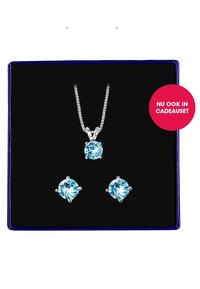 Zilveren sieradenset met een hangerketting voorzien van een lichtblauwe edelsteen en bijpassende studoorbellen, weergegeven op een zwart fluwelen achtergrond.