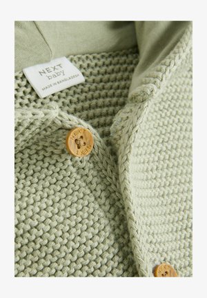 Svetle zelený pletený svetr se strukturovaným vzorem, hladkým límečkem a dřevěnými knoflíky s vygravírovaným názvem značky. Štítek nese nápis "NEXT baby).