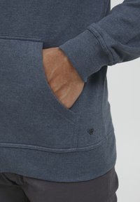 Sweat à capuche bleu marine en tissu doux, avec une poche kangourou, des poignets côtelés et un petit logo noir en détail au bas.