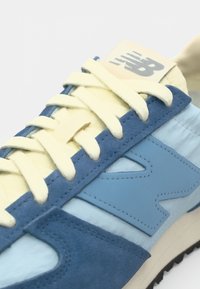 Blue suede and synthetic low-top sneaker with cream laces and accents. Features a blue logo on the side and a textured outsole.