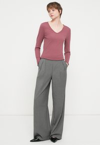 Langermet, stripete, plommefarget v-hals topp med bølget kant, kombinert med høy midje, vide, grå dressbukser. Fottøyet er skinnende svarte sko.