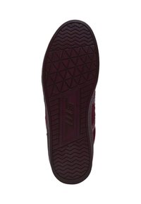 Sole of a burgundy sneaker featuring textured rubber, with a geometric tread pattern and a central logo accent.