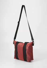 Sac en synthétique rouge avec des sangles en nylon noir, forme rectangulaire, texture lisse, fermeture zippée et deux grosses bandes verticales sur le devant.