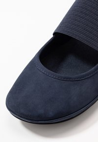 Gros plan d'une chaussure plate bleu marine au bout arrondi et à large bande élastique sur le dessus pour un maintien sécurisé.