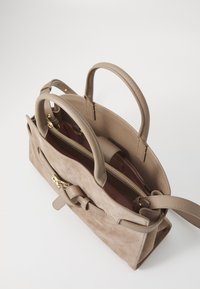 Sac à main en daim et cuir beige avec deux poignées courtes et une bandoulière amovible. Il dispose d'un compartiment principal zippé et d'une poche intérieure.