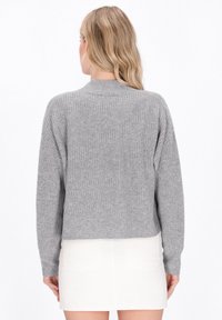 Grijze geribbelde gebreide trui met een ronde hals en lange mouwen. Heeft een cropped lengte en een gestructureerde stof. Draag het over een witte rok.