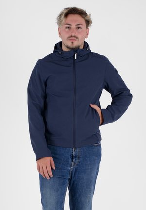 Marineblauwe ritsjack met capuchon, met een gladde textuur, een getailleerd ontwerp en een klein logo op de linkermouw. Geddragen met blauwe jeans.