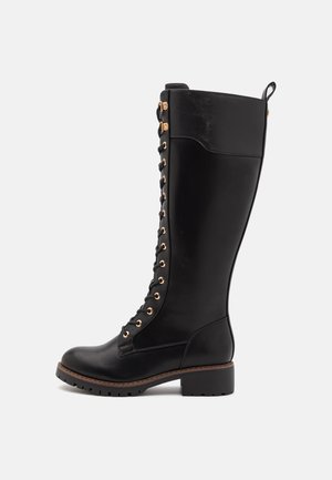 Čierne kožené čižmy po kolená so šnurovaním, so zlatými očkami, textúrovaným povrchom a masívnym podpätkom.