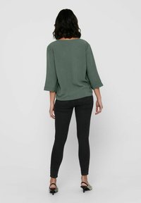 Groene, losse top met driekwart mouwen, gecombineerd met zwarte skinny jeans. De top heeft een eenvoudig ontwerp en een ronde halslijn.