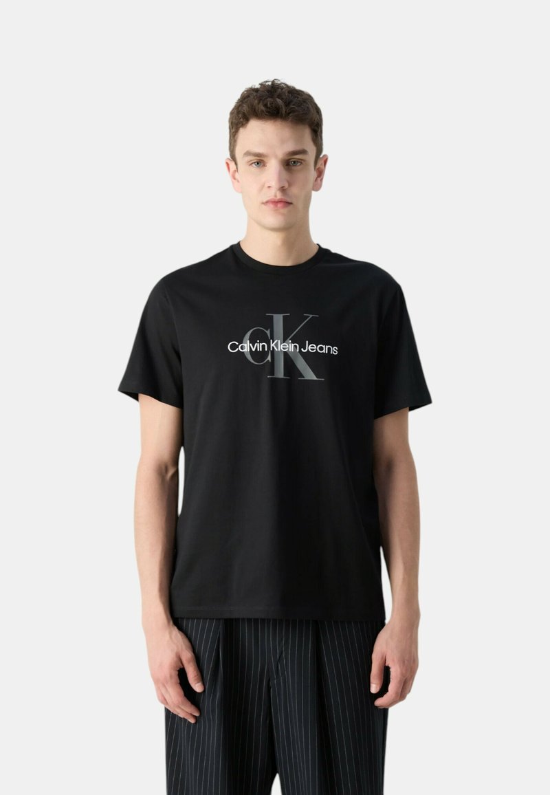 Camiseta de algodón negra con un logo en blanco y gris de "Calvin Klein Jeans". Mangas cortas, escote redondo, combinada con pantalones a rayas.