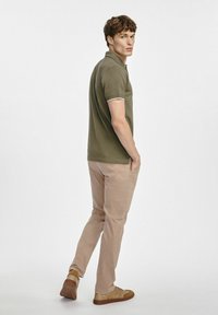 Oliwkowa koszulka polo z białymi wstawkami, zestawiona z jasnobeżowymi chinosami i brązowymi trampkami, prezentująca prosty, casualowy styl.