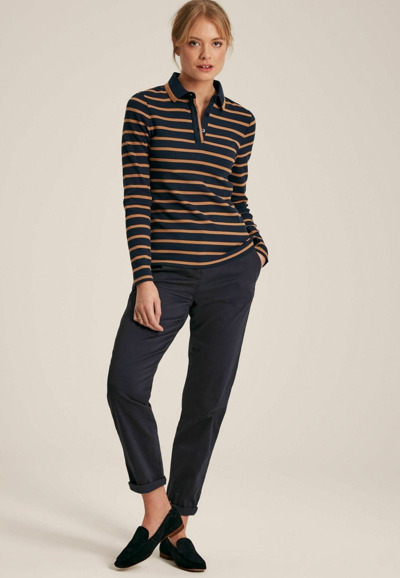 Marineblaues Langarm-Polohemd mit dünnen hellbraunen Streifen, mit Kragen und Knöpfen, kombiniert mit dunklen Hosen und schwarzen Slippern.