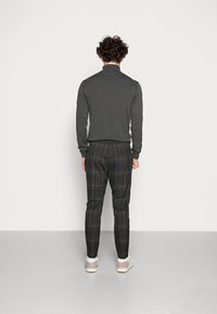 Ciemnoszary top z długim rękawem w połączeniu z kratkowymi spodniami w czarno-żółto-białych kolorach; biały sneakers dopełnia stylizację.