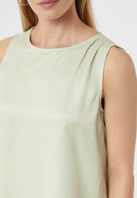 Jasnozielony top bez rękawów z gładkiego materiału, posiadający okrągły dekolt i fałdowane detale na ramionach. Prosty, czysty design.