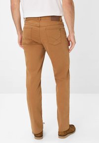 Pantaloni di cotone marroni con un design a gamba dritta, caratterizzati da tasche posteriori e dettagli di cucitura sottili, abbinati a scarpe in suede marroni.
