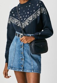 Marinblå sweatshirt med vit mönstrad design, kombinerad med en ljus denimkjol med knappar framtill och en liten svart crossbody-väska.