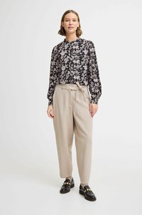 Blusa a fantasia floreale nera e beige con maniche lunghe e dettaglio dei bottoni, abbinata a pantaloni beige a vita alta e mocassini neri.